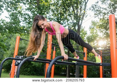 Low-angle view of a cheerful beautiful woman passionate about calisthenics training exercising basic plank position outdoors in a modern fitness park