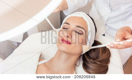 High-angle close-up view of the face of a beautiful woman during anti-aging facial massage with soft brushes in a modern cosmetic center