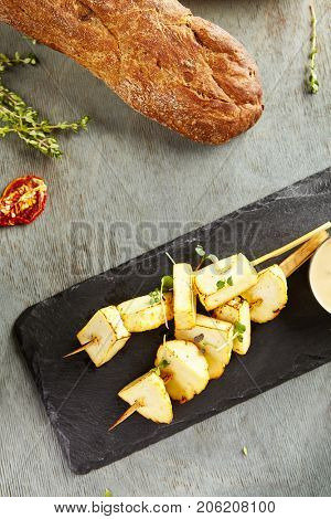 Hot appetizer - fried cheese halumi on wooden stick on black stone against of blurry bread. Gastronomic restaurant menu. Top View