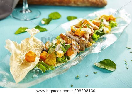 Menu of gastronomic restaurant. Warm salad with chicken baked pumpkin and cheese halumi with fresh herbs on  glass plate on  blue wooden table