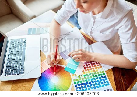 Creative designer pointing at color diagram while making choice from palette swatches