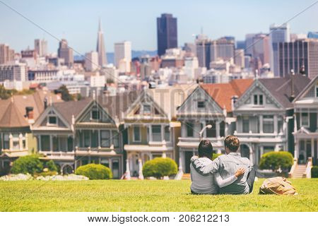 San Francisco - Alamo Square people. Couple tourists relaxing in Alamo Park by the Painted Ladies houses iconic landscape, The Seven Sisters, San Francisco, California, USA.