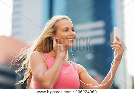 technology, lifestyle and people concept - smiling young woman with smartphone and earphones listening to music and taking selfie in city