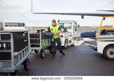 Male Worker Placing Luggage In Trailer On Runway