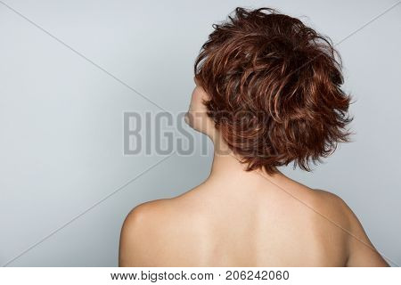 Beautiful young woman with short pixie haircut with her back to the camera on the grey studio background