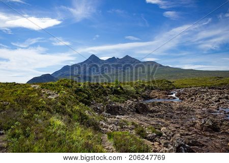 Mountain peaks of the Black Cuillins and Tir Nan Iolaire or the Land of Eagles with a drying riverbed and slight stream running through.