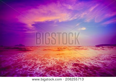 Beautiful tropical sunset in Krabi, Thailand. Dramatic and picturesque evening scene. Ocean waves and colorful cloudy sky in the background. Nature landscape. Travel background. Bright purple toning