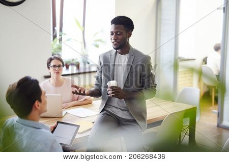 Multi-ethnic team of talented designers gathered together at spacious boardroom and having productive discussion of joint project, African American colleague expressing his point of view