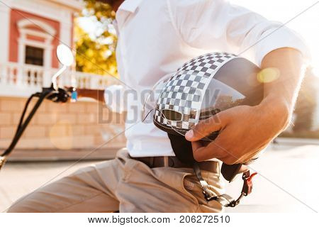 Cropped image of young african man sitting on modern motorbike and holding moto helmet outdoors