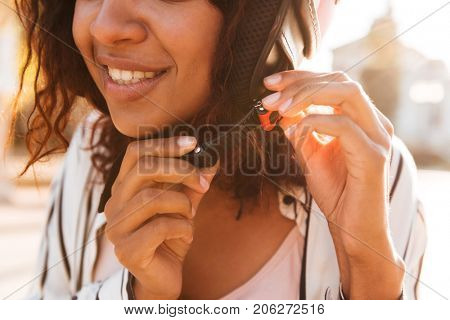 Cropped picture of happy african woman fastens her moto helmet outdoors