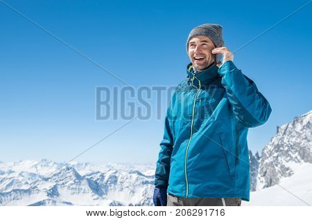 Portrait of a young man talking on mobile phone on snowy mountain. Happy guy using cellphone in winter holiday with copy space. Smiling man has a joyful conversation at phone.