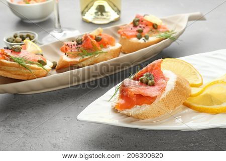 Tasty small sandwiches with salmon and capers on plates