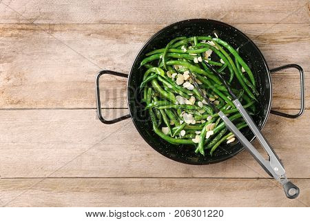 Frying pan with delicious green beans and almond on wooden background