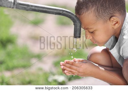 African American child drinking water from tap outdoors. Water scarcity concept