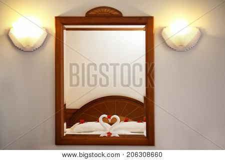Bed with towel swans and floral decor reflecting in hotel room mirror