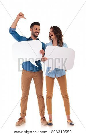 laughing casual couple holding speech bubbles , man is pointing to his woman on white background