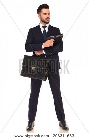 young modern hitman showing his gun while standing with suitcase on white background