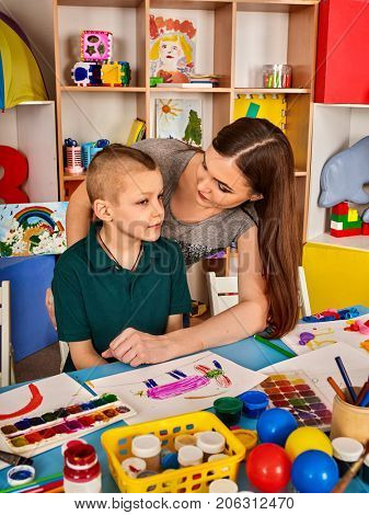 Small students girl and boy with teacher painting in art school class. Child drawing by paints on table. Mom praises son in kindergarten. Preparing for a children's art exhibition.