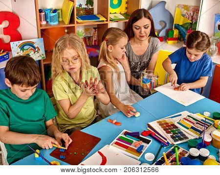 Plasticine modeling clay in children class. Teacher teaches kids together play dough and mold from plasticine in kindergarten or preschool. Group of four people. Zoo from the clay.