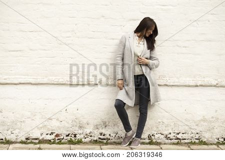 Portrait of a full length brunette woman in a gray woolen coat in a stone wall of white brick