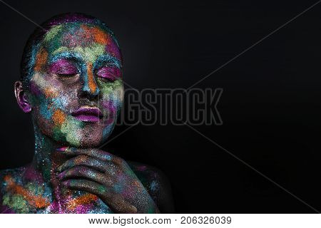 Young artistic woman in black paint and colourful powder. Glowing dark makeup. Creative body art on the theme of space and stars. Bodypainting project: art, beauty, fashion