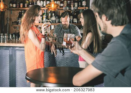 Handsome drunk man sitting at bar, drinking cocktail and looking at two attractive girls. He wants to get to know them, but does not know how. Nightclub. Date