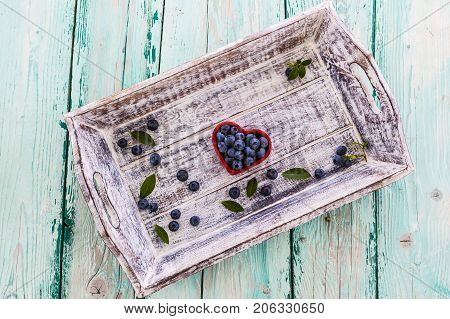 Fresh blueberries in a bowl in the shape of a heart on a wooden background.