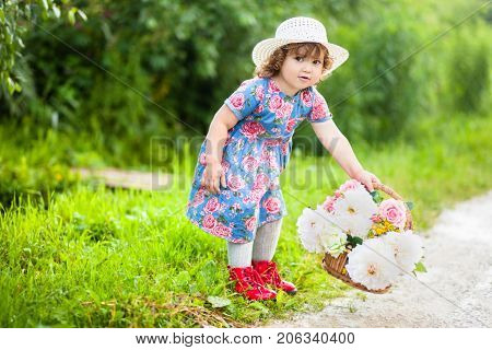 Adorable little curl hair girl walking with the basket of flowers in a summer day.