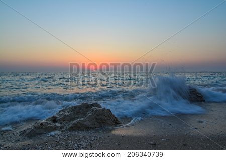 Sunset on a beach splashing waves sand rocks and sun on horizon in twillight