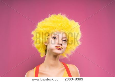 funny girl in bright yellow wig with chupa chups smiles into the camera