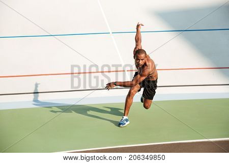 Full length portrait of a half naked motivated sportsman starting to run on a track field outdoors