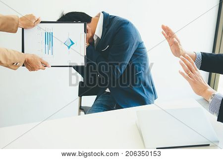 Angry boss giving a document to a sad employee sitting in a desk at office