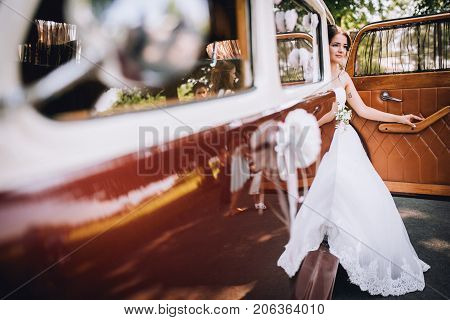Beautiful girl sitting in a retro car. Brunett bride portrait with flowers.
