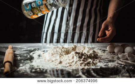 Man makes dough from flour and eggs on a glass table