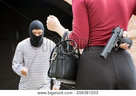 Male robber standing and looking at young woman and young woman hide gun in his back/self-defense of woman,criminal concept