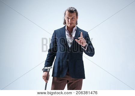 The mature bearded man in a suit holding cane. Isolated on a blue studio background.