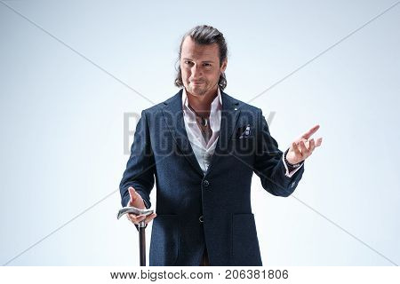 The mature bearded man in a suit holding cane. Isolated on a blue studio background.