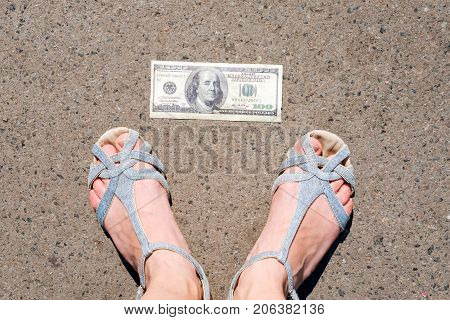 Lucky woman finding money on the street. Women feet next to hundred dollar bill. Lost and found money lying down on asphalt road
