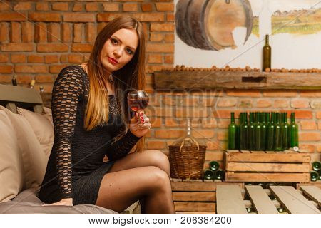 Elegant beauty lady long hair full make up wearing black dress tasting wine in rural cottage interior celler