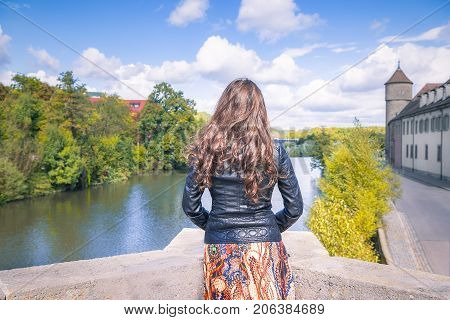 Young woman with the backside at the camera on the edge of a bridge watches towards the horizon meditating in Schwabisch Hall Germany.