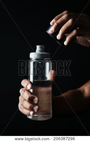 Cropped photo of afro american males hands opening the bottle with water , isolsted on black background