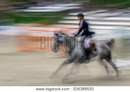 Abstract image with a moving rider and horse at show jumping on blurred background.