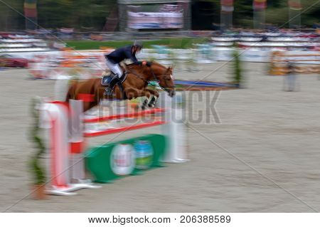 Abstract image with a moving rider and horse at show jumping on blurred background.