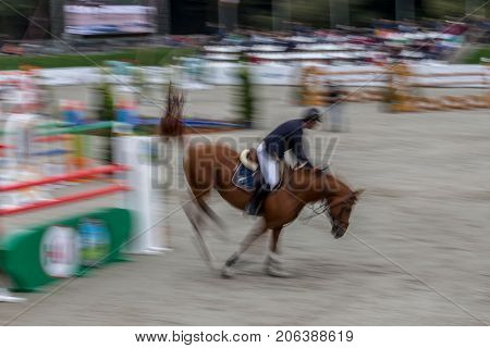 Abstract image with a moving rider and horse at show jumping on blurred background.