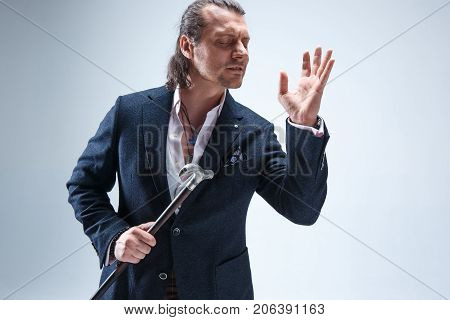 The mature bearded man in a suit holding cane. Isolated on a blue studio background.