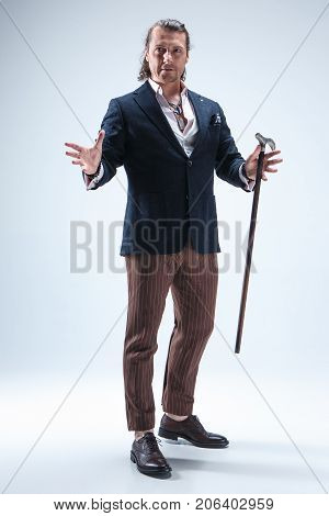The mature bearded man in a suit holding cane. Isolated on a blue studio background.