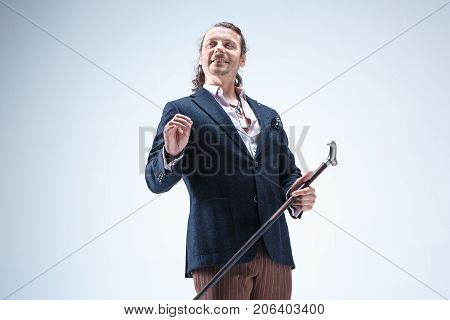The mature bearded man in a suit holding cane. Isolated on a blue studio background.