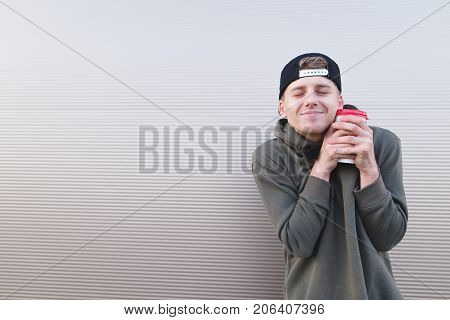 A funny young man hugging a cup of coffee on a light background