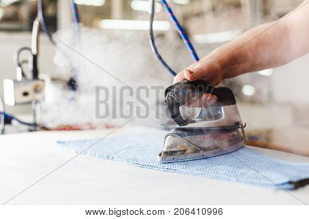 Professional ironing in dry cleaner detail of iron and hands. Presser in sewing clothes pressed