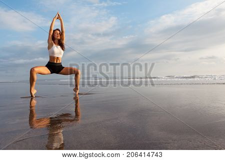 Meditation on sunset sky background. Young active woman in yoga pose on sea beach stretching to keep fit and health. Healthy lifestyle outdoor fitness sports activity on summer family holiday.